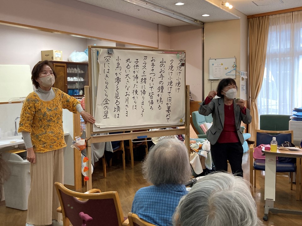 コラムやエッセイなどの朗読、歌と伴奏、手遊びなどで、<br>ご利用者のみなさんを楽しませてくださいます。<br>代表の千葉明子さんは教会の聖歌隊に属されていて、『ふるさと』や『七つの子』などを<br>指揮をされ、梶原さんの伴奏でみなさんと歌って下さいました。<br>